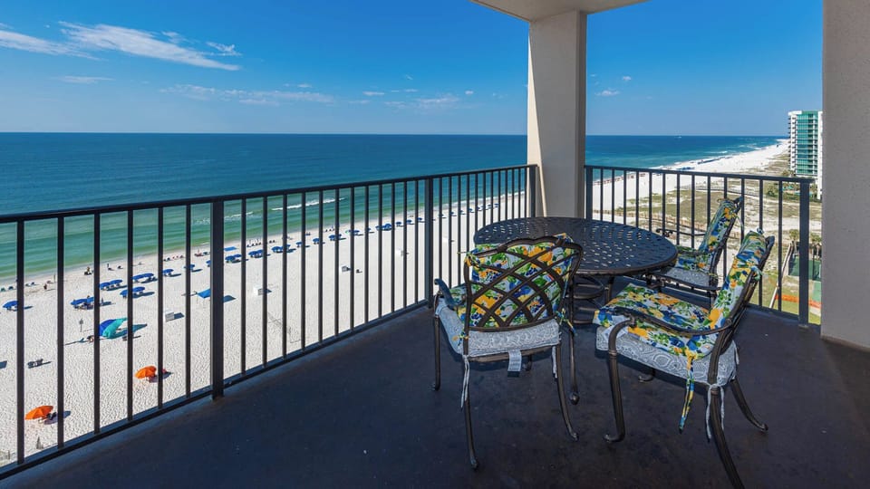 Relax on the balcony with colorful seating, enjoying panoramic views of the beach and gentle waves below