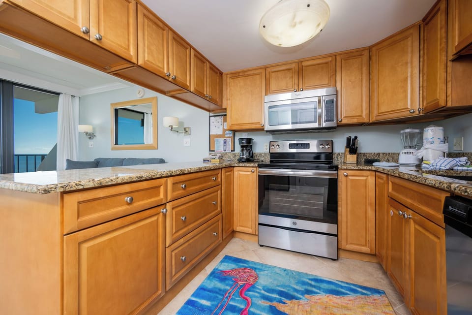 This kitchen features modern appliances, granite countertops, and a cozy seating area with a view of the beach