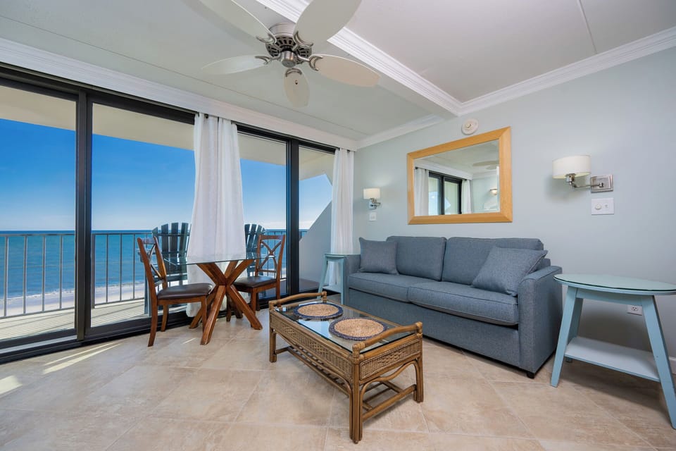This inviting seating area features a comfortable sofa and a glass-top table with stunning beachfront views