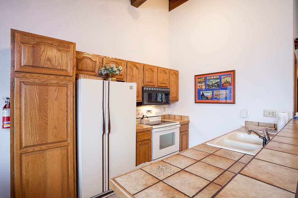 Your fully-equipped kitchen features beautiful wood cabinetry, stainless appliances, and spacious tile countertops perfect for preparing memorable meals during your stay.