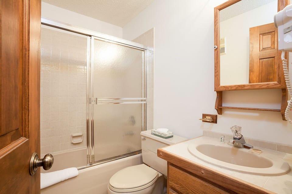 Step into a bright, spotless bathroom featuring warm oak cabinetry, fresh towels at your fingertips, and a tub-shower combo ready for relaxing soaks or quick refreshes after adventurous days.