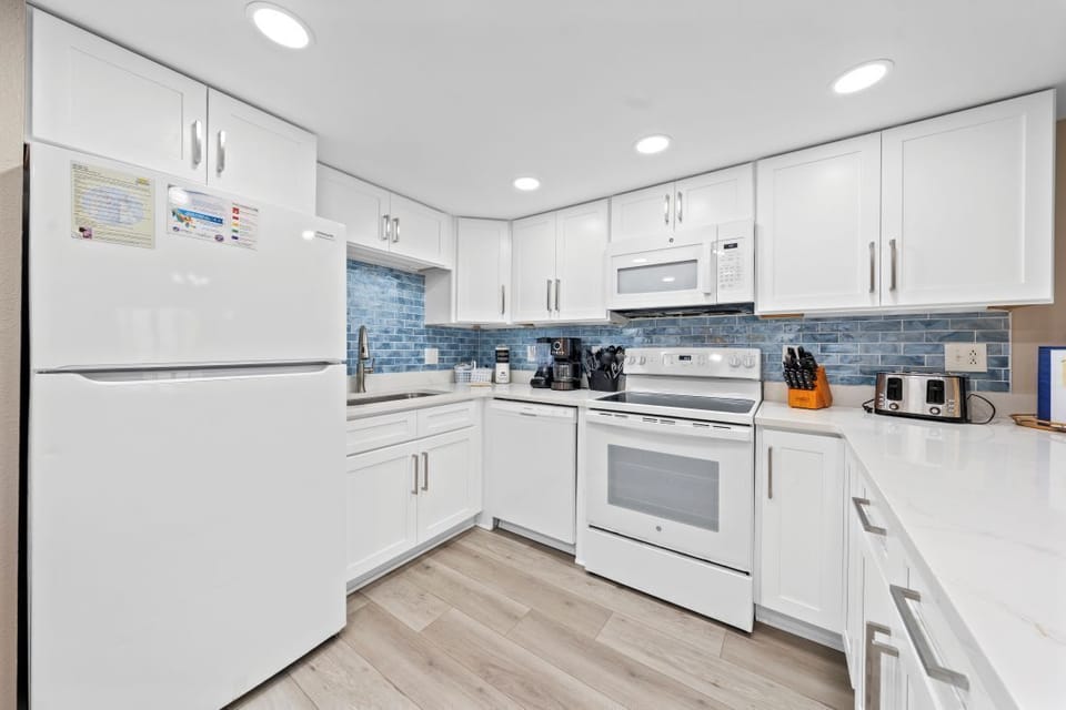 Your fully equipped kitchen awaits with crisp white cabinets, beautiful blue tile backsplash, and modern appliances ready for cooking memorable meals.