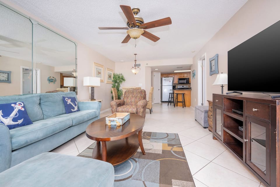 The living area features a blue sofa with anchor pillows, a patterned chair, and a large TV, creating a relaxed atmosphere