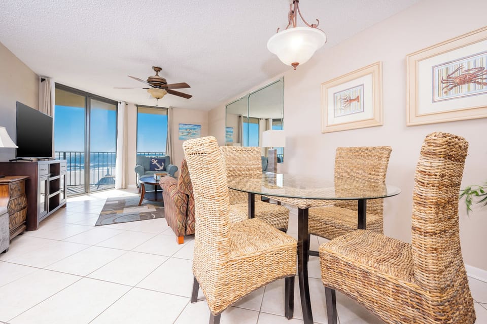 Living area featuring a glass dining table with woven chairs, a cozy sofa chair, and expansive views of the beach