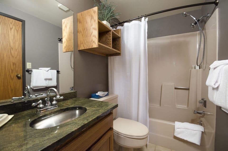 Your private bathroom has everything you need—plush towels, a clean shower/tub combo, and a spacious vanity with warm wood finishes that invite you to unwind.