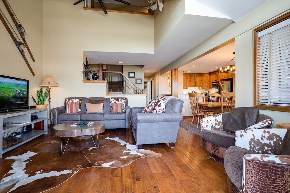 Relax in your spacious living area with cowhide rug, comfortable seating, and warm wood accents creating the perfect mountain retreat atmosphere.
