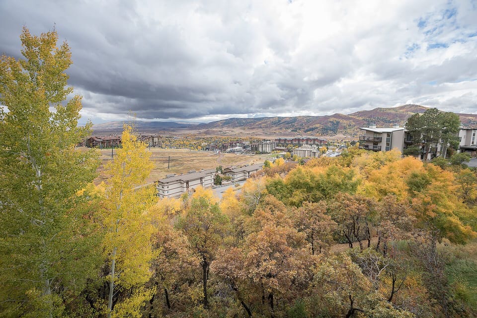Elevated view showcasing vibrant autumn foliage across the valley, with distant mountains and surrounding residential areas creating a scenic mountain town setting.