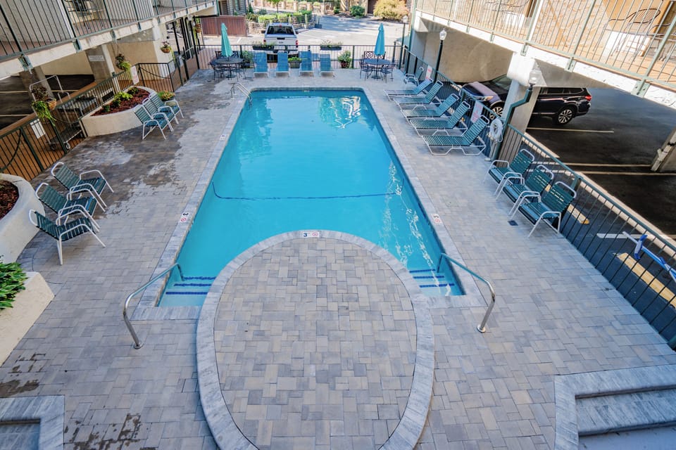 The property features a refreshing outdoor pool area with ample lounge seating, surrounded by paver decking and convenient parking nearby.