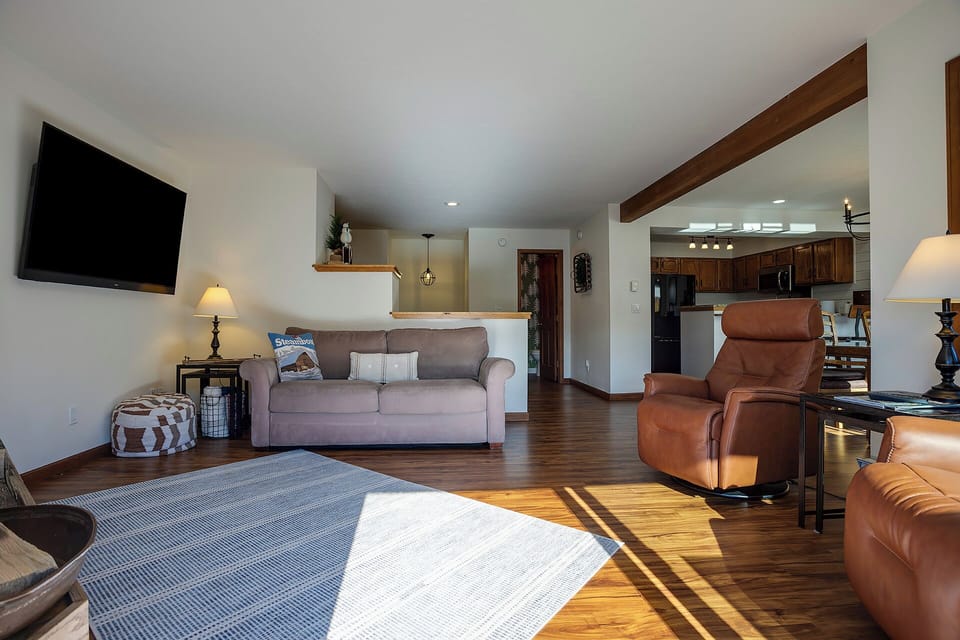 Settle into your spacious living room where warm wood beams frame comfortable seating and natural light dances across gleaming floors.