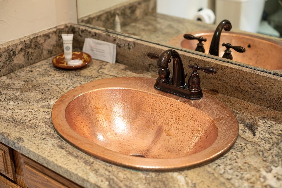 Unwind in your private bathroom featuring a stunning copper sink and granite counters, with premium amenities awaiting your arrival.