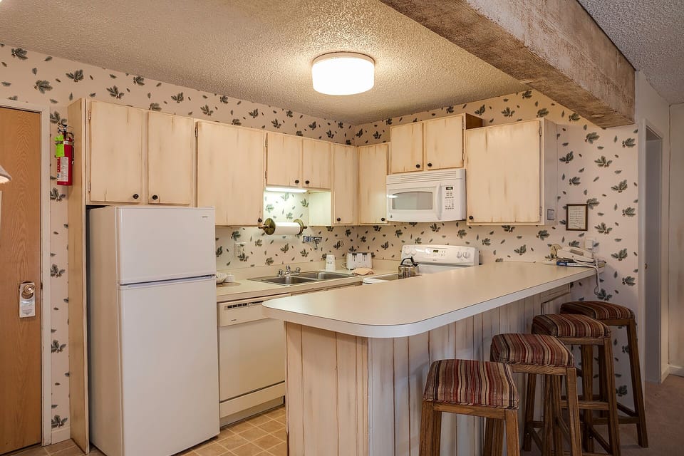 Your cozy kitchen features rustic charm with leafy wallpaper, warm wood beams, and everything you need to prepare meals during your stay.