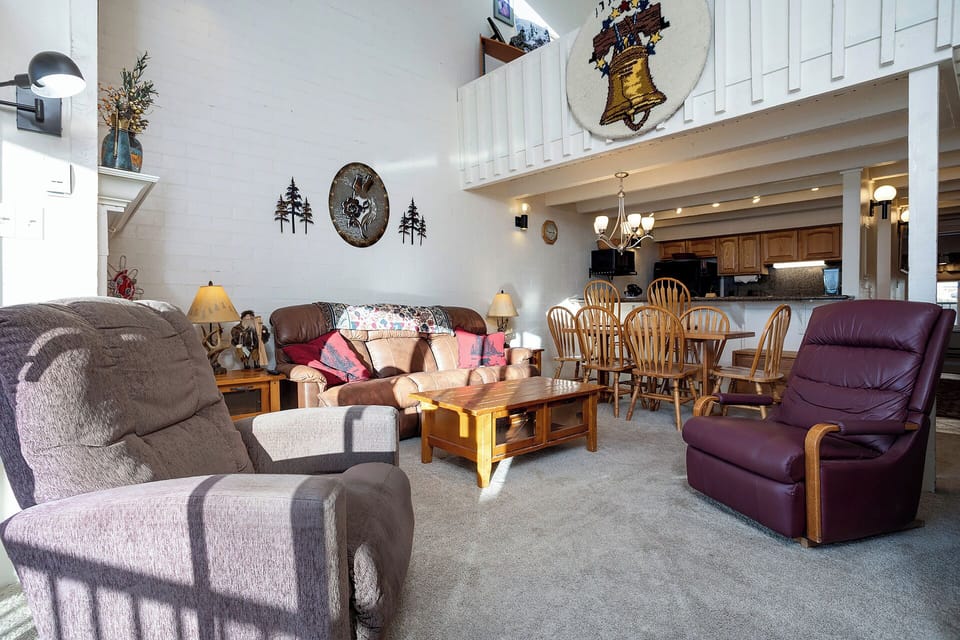 Relax in your spacious open-concept living room featuring comfortable leather seating and rustic mountain charm with soaring ceilings and loft views.