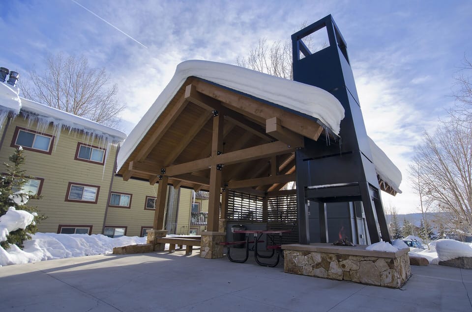 Mountain retreat features a covered outdoor pavilion with fireplace and BBQ area, perfect for winter gatherings amid snowy alpine scenery.