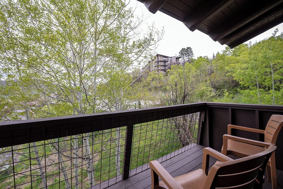 Relax on your private balcony with wooden chairs, overlooking peaceful greenery and distant mountain homes.