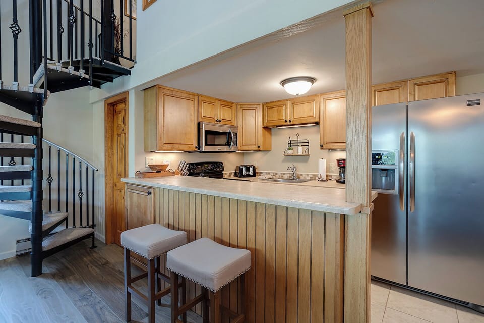 Your fully equipped kitchen features warm wood cabinetry, stainless steel appliances, and a breakfast bar perfect for morning coffee or evening snacks.