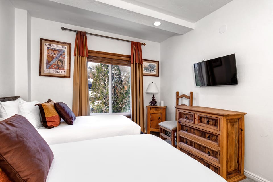 The second bedroom has two twin beds, wooden dresser, and flat screen TV mounted to the wall.