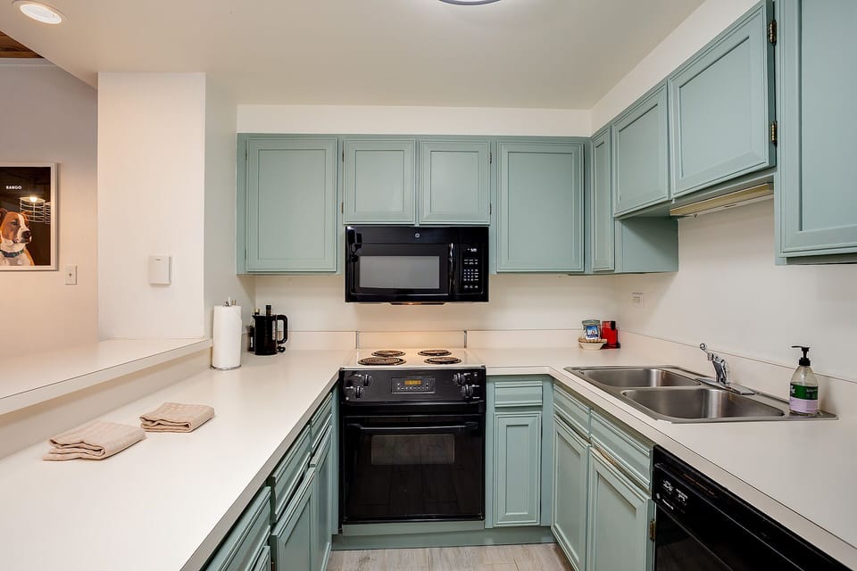 Your fully equipped kitchen awaits with sage-green cabinets, white countertops, and modern appliances ready for home cooking.