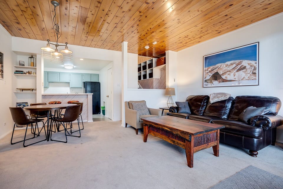 Relax in your stylish open-concept living space with rustic wood ceiling, leather sofa, and mountain artwork creating the perfect alpine retreat atmosphere.