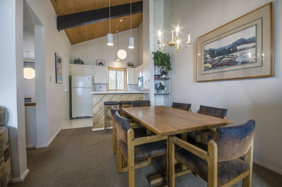 Your spacious dining room features a solid wood table perfect for family meals, with modern kitchen and soaring ceilings creating an inviting atmosphere.