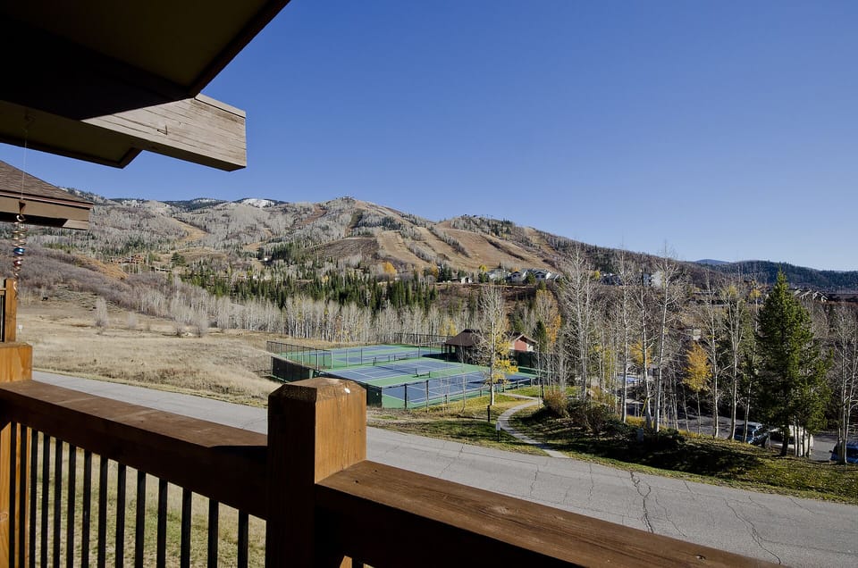 Mountain resort view featuring tennis courts and ski slopes set against dramatic peaks and autumn foliage.