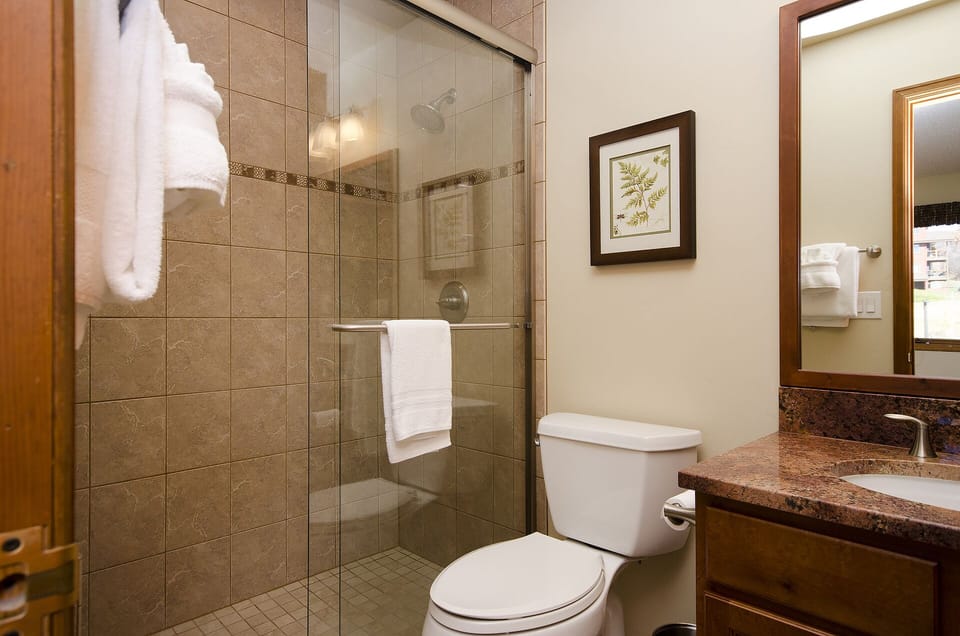 Your private bathroom features warm travertine tile, a sleek glass-enclosed shower, and plush towels ready to wrap you in comfort after a refreshing rinse.