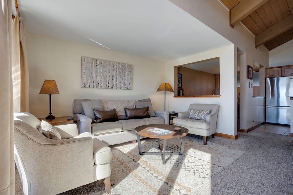 Unwind in your spacious living room where natural light streams across plush seating and warm wood beams create a cozy mountain retreat atmosphere.