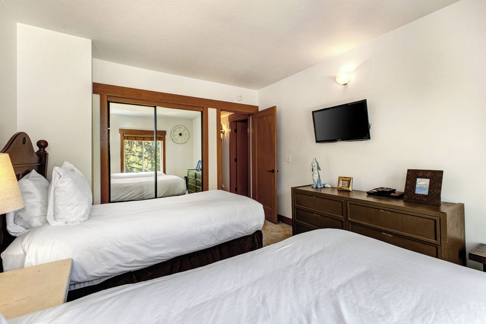 Park Station 134's second bedroom with two twin beds, mirrored closet doors, dark wood dresser, wall mounted TV and window.
