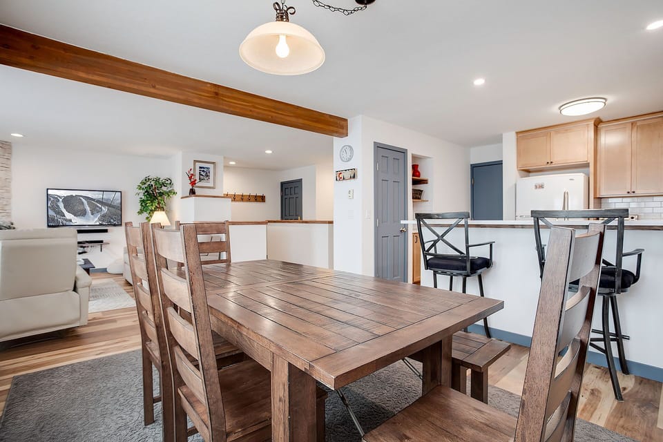 Gather around the rustic dining table where morning coffee conversations and evening meals create lasting memories in this open, light-filled space.