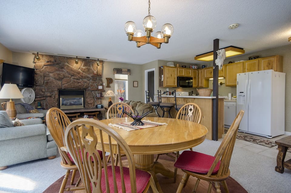 Gather around your spacious dining table with loved ones in this warm, open-concept space featuring a cozy stone fireplace and fully-equipped kitchen.