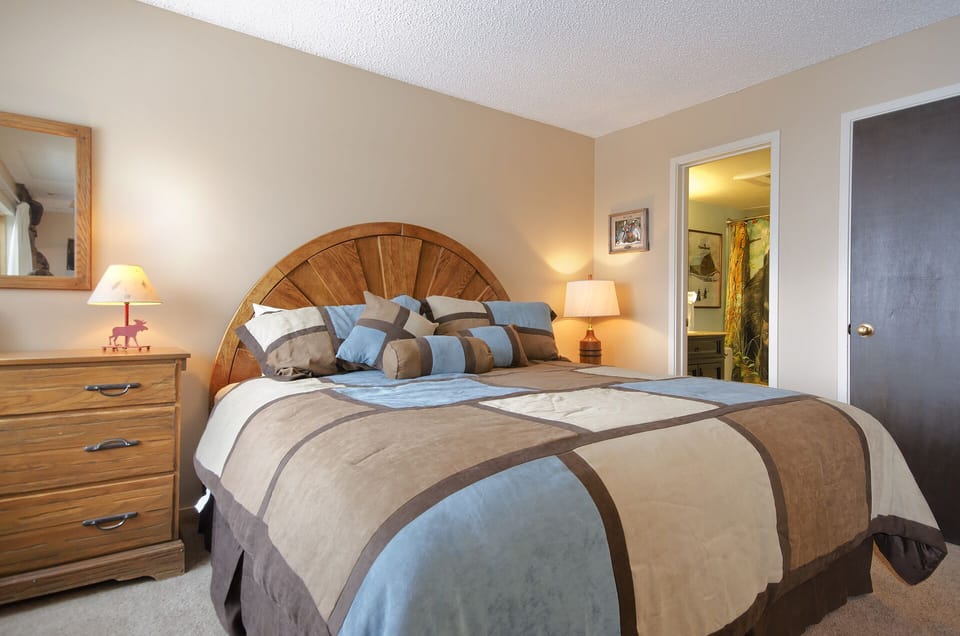 Sink into your cozy bedroom retreat with its distinctive wooden headboard and soft blue-brown bedding, promising restful nights in comfort.