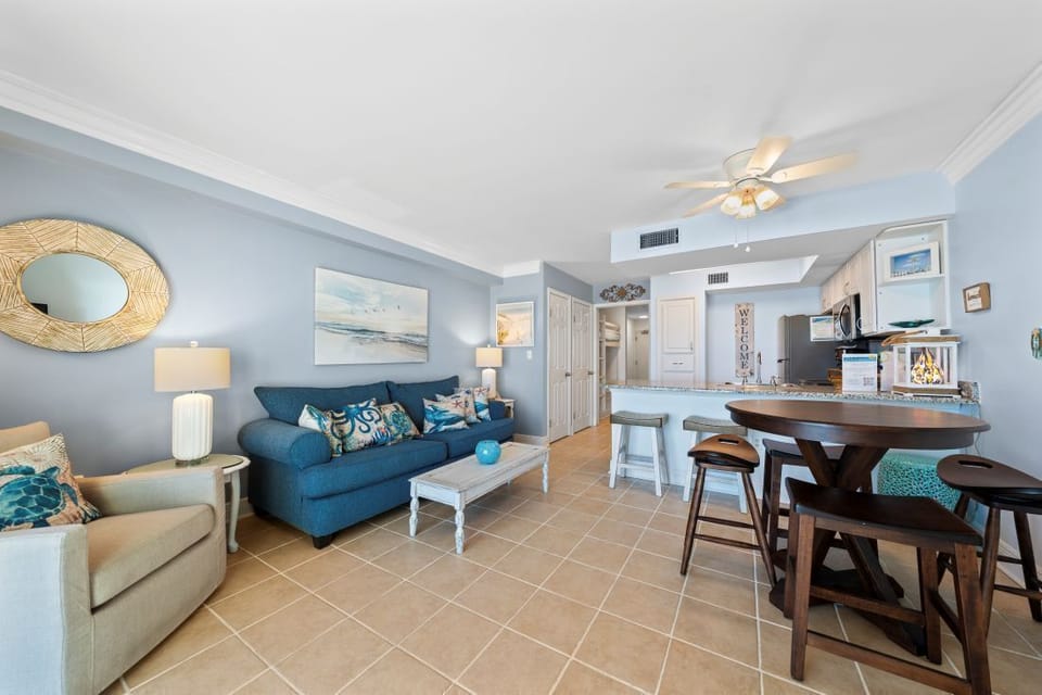 Relax in your coastal-inspired living space with soothing blue tones, comfortable seating, and an open kitchen perfect for preparing meals together.
