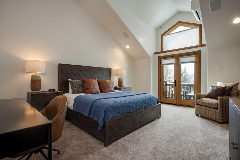 Sink into your luxurious mountain retreat bedroom, where vaulted ceilings and French doors create an airy sanctuary for restful nights.