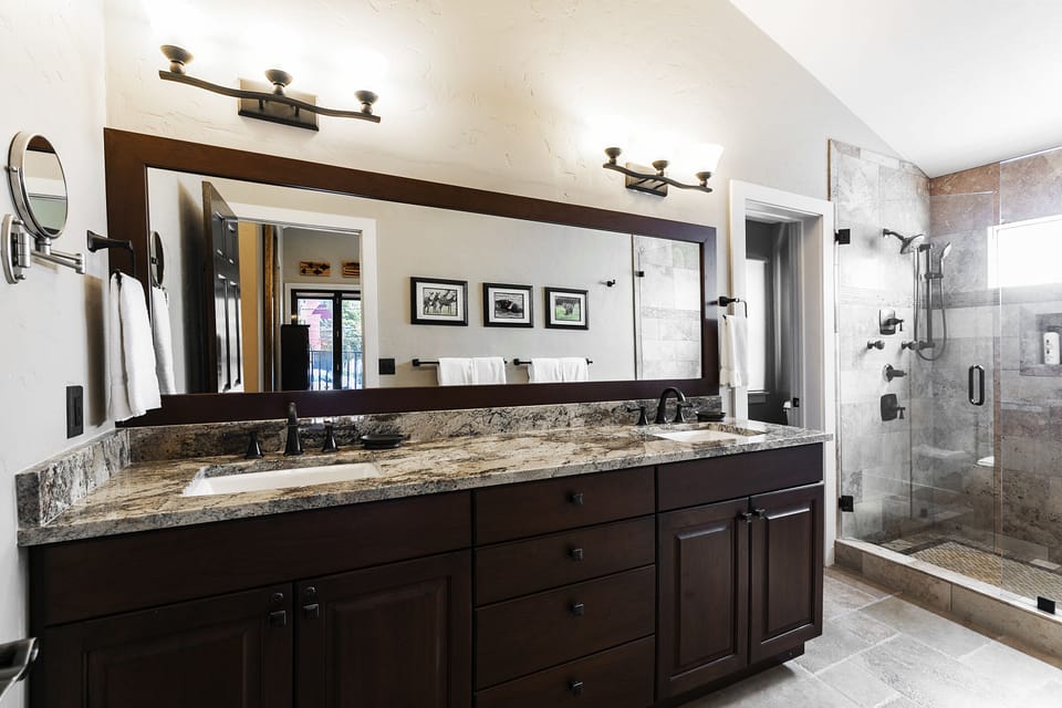 En-suite main bathroom with granite countertops, dual vanity, glass shower door