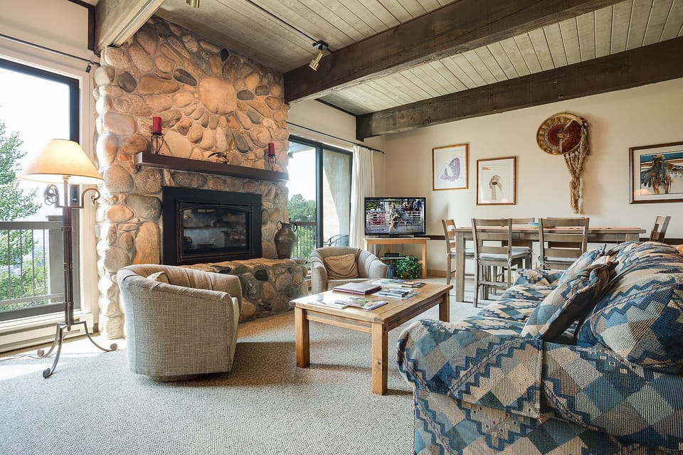 Cozy living room with stone fireplace, exposed beams, and mountain views creates your perfect retreat for relaxation.