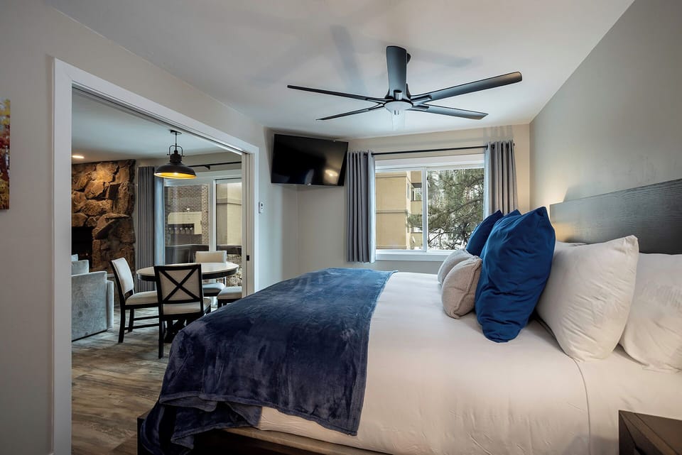 Sink into plush bedding with royal blue accents in your spacious bedroom, where a ceiling fan keeps you cool and adjacent living space invites relaxation.