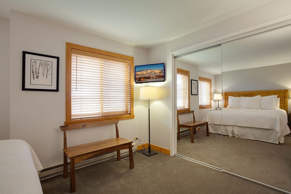 Your peaceful bedroom features warm wood accents, soft natural light through blinds, and a cozy seating bench—perfect for unwinding after mountain adventures.