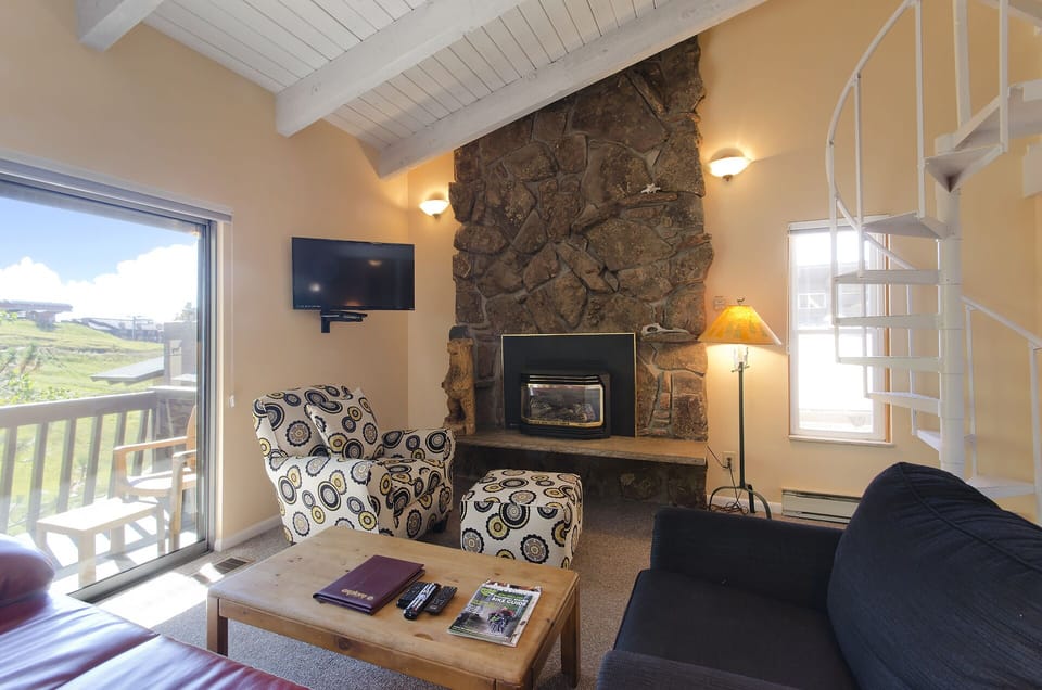 Curl up by your stone fireplace with mountain views streaming through expansive windows in this cozy living space.