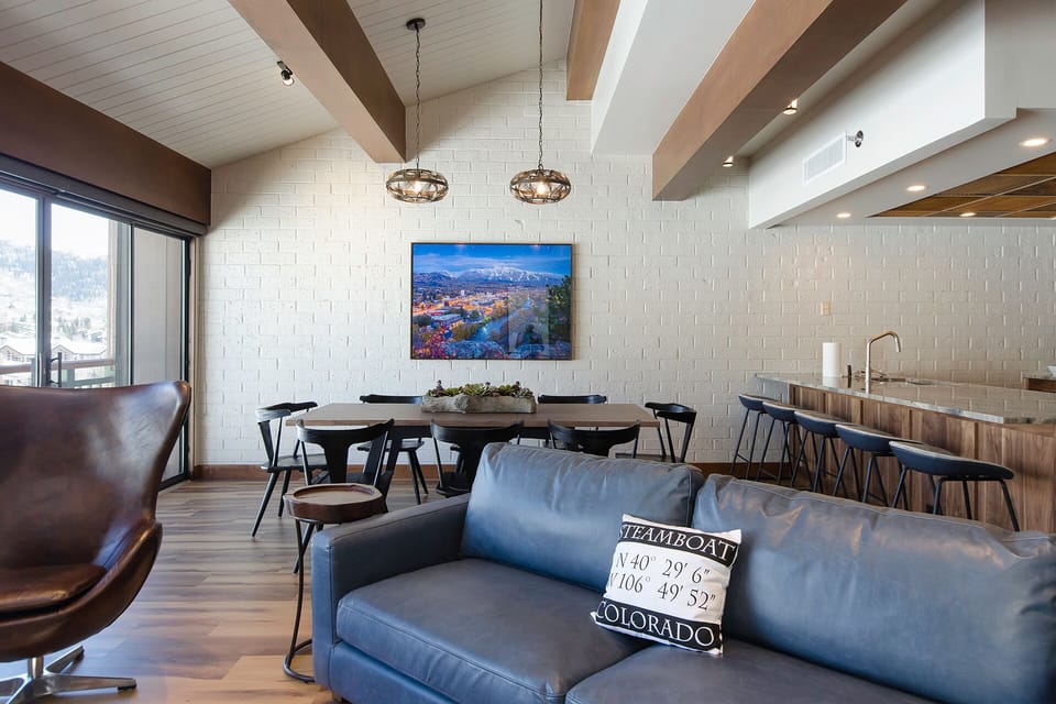 Your open-concept space flows seamlessly from living to dining to kitchen, featuring exposed beams, leather seating, and mountain views.
