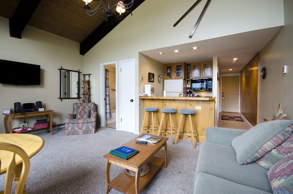 Unwind in your cozy open-concept retreat with rustic exposed beams, a fully equipped kitchen, and comfortable seating perfect for mountain getaways.