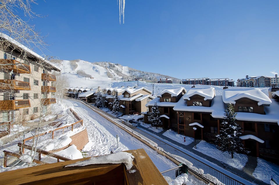 A pristine winter alpine village nestled beneath snow-covered slopes, showcasing traditional mountain architecture and ski resort amenities in the surrounding area.