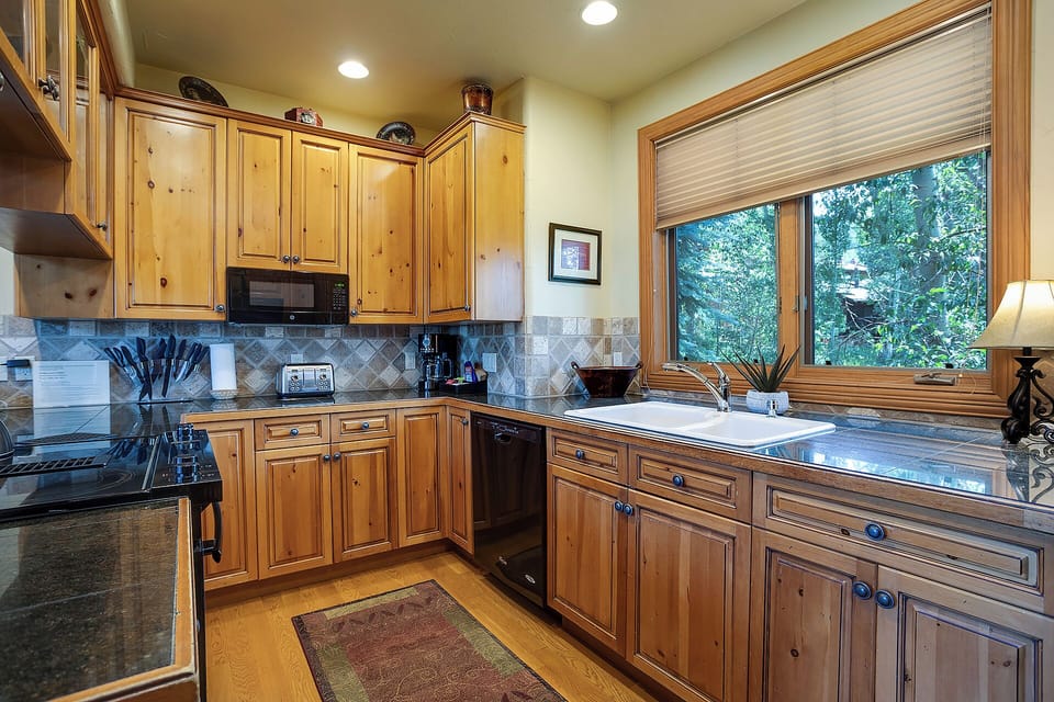 Cook in your well-appointed kitchen with warm wood cabinets, granite counters, and forest views through the window.