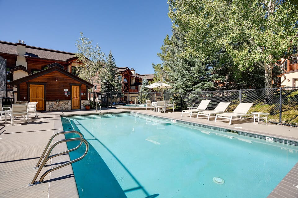 Sparkling shared pool surrounded by mountain resort buildings and mature trees, perfect for relaxing summer days.