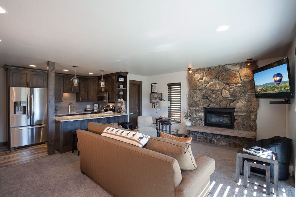 Cozy up in your open-concept living space featuring a stunning stone fireplace, modern kitchen, and comfortable seating perfect for evening relaxation.
