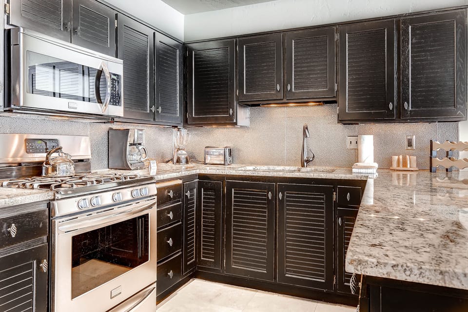 Queen Esther's kitchen has black painted wood cabinets, granite counters and stainless steel appliances.