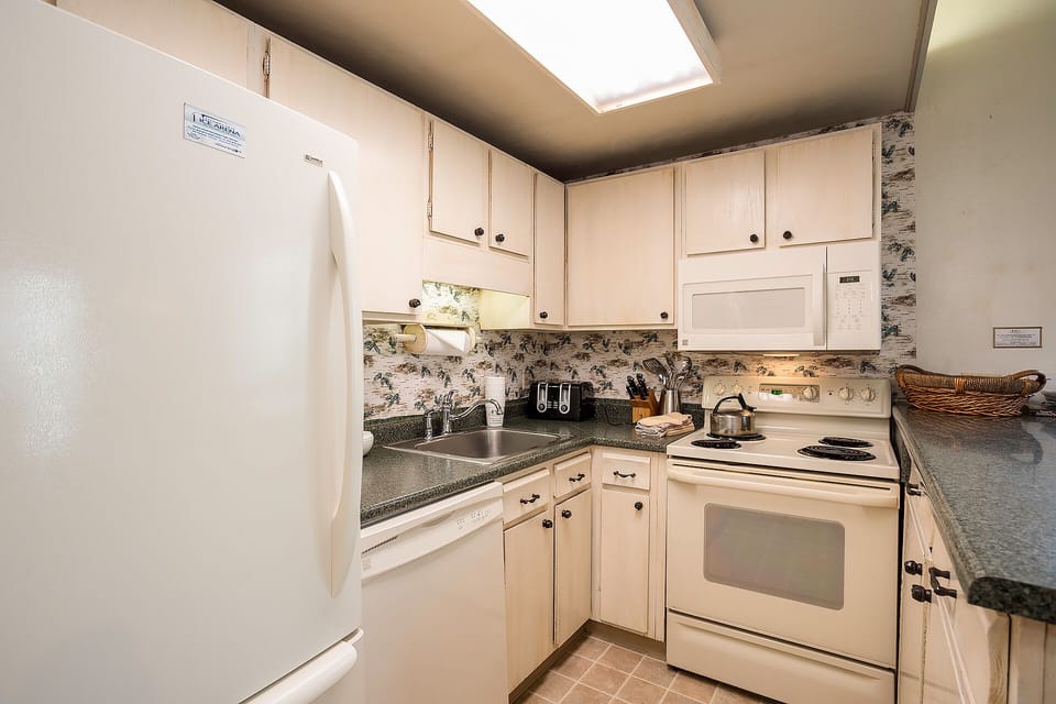 Your fully-equipped kitchen features granite countertops, white appliances, and charming toile backsplash for preparing memorable meals during your stay.