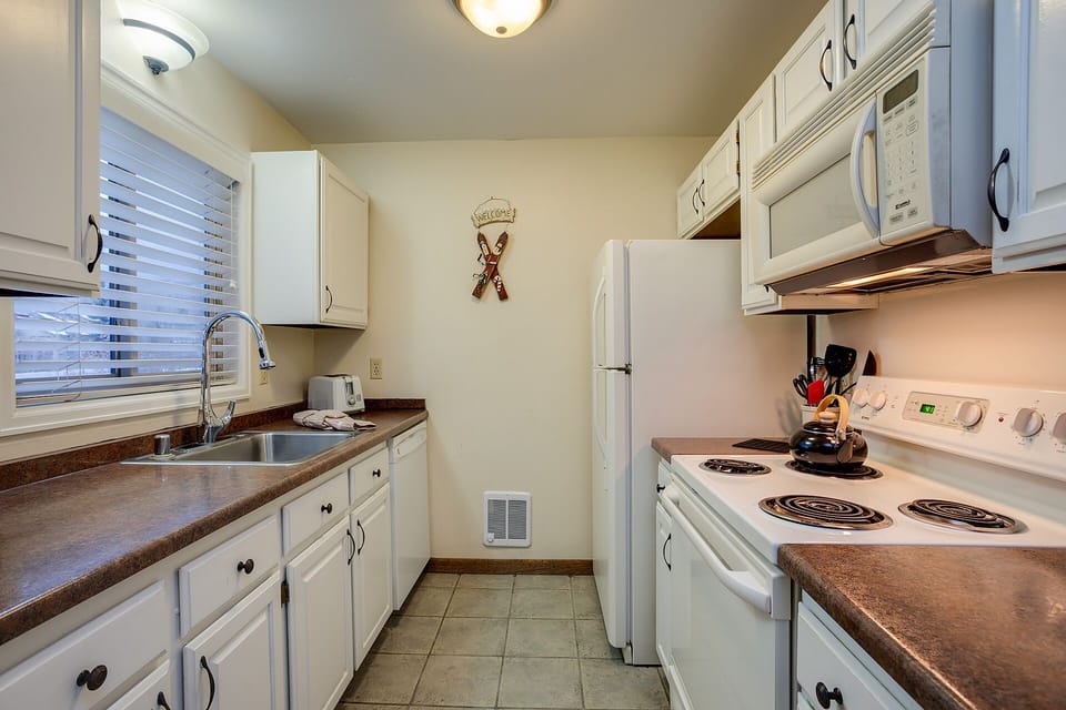 Your fully equipped galley kitchen features everything you need for home-cooked meals, with white appliances and warm countertops creating a welcoming culinary space.
