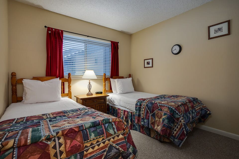 Settle into your cozy twin bedroom with comfortable beds, warm lighting, and cheerful red curtains creating the perfect retreat.