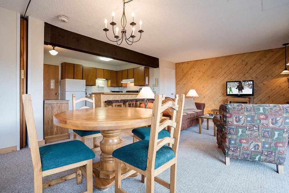 Gather around the warm wooden dining table where rustic beams meet modern comfort in your mountain retreat's open living space.