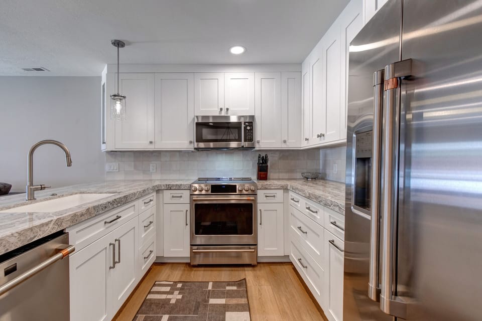 White kitchen cabinets, with grey counters and stainless steel appliances.