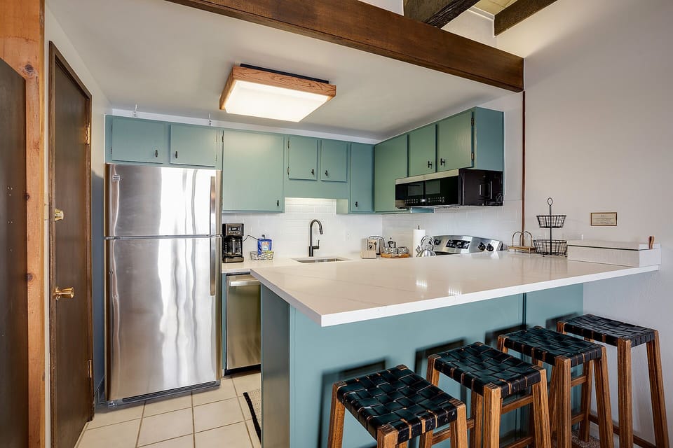 Your kitchen features beautiful exposed beams, sage-green cabinetry, and modern appliances—perfect for preparing meals while soaking in the cozy charm.